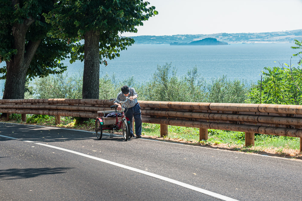 Old man pushing bicycle up hill in Italy